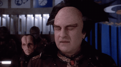 Bald Man Standing In Front Of Blue Curtain With Clock GIF