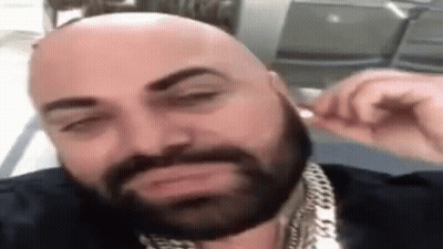 Bald Man With Beard And Chains Adjusting Earbuds GIF