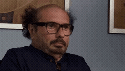 Bald Man With Beard And Glasses Sitting In Front Of Picture GIF