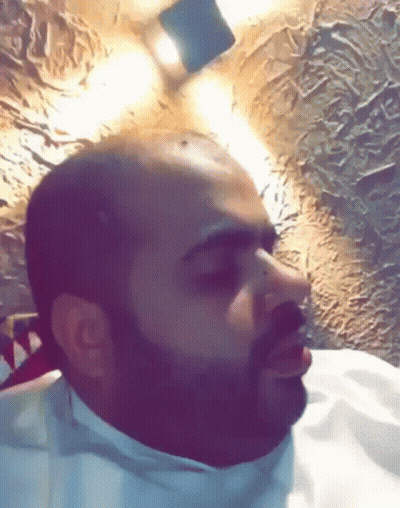 Bald Man With Beard Sitting In Front Of Lit Wall GIF