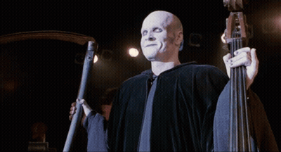 Bald Man With White Face Paint Holding Scythe On Stage GIF