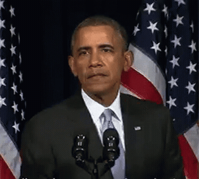 Barack Obama Is Giving A Speech In Front Of A Microphone In Front Of American Flags . GIF