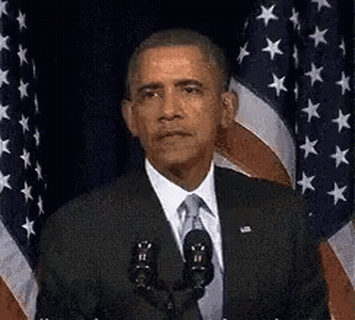 Barack Obama Is Giving A Speech In Front Of A Microphone In Front Of An American Flag . GIF