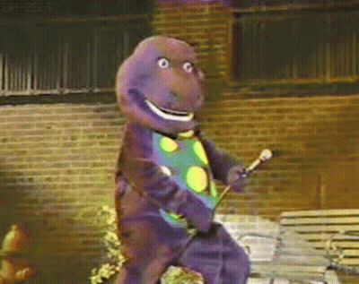 Barney The Dinosaur Is Holding A Microphone And Dancing In Front Of A Brick Building GIF