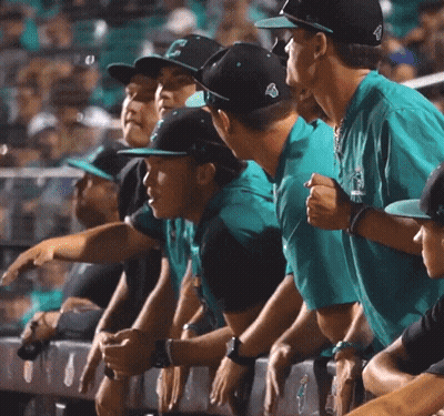 Baseball Players In Teal Shirts And Black Hats Watching Game GIF