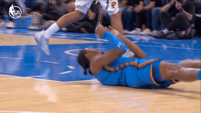 Jugador de baloncesto tumbado en el suelo mientras otro salta sobre él GIF
