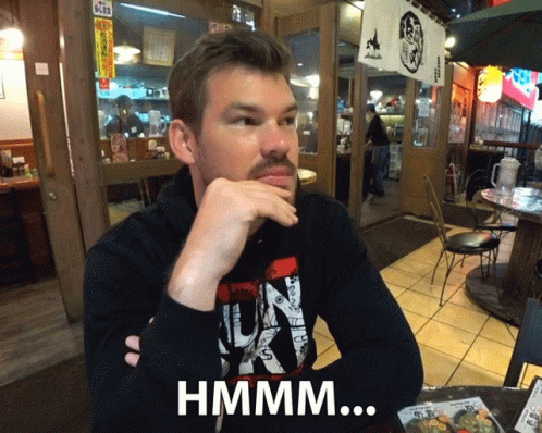 Bearded Man At Table With Hand On Chin Hmmm Sign GIF