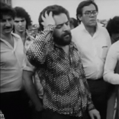 Bearded Man Holding Hand To Head In Crowd GIF