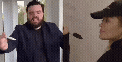 Bearded Man Holding Pen Next To Woman In Hat GIF