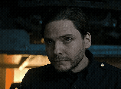 Bearded Man In Black Shirt Looking At Camera In Dark Room GIF