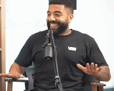 Bearded Man In Black Vans Shirt Talking Into Microphone GIF