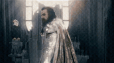 Hombre barbudo con capa de pie en una habitación oscura GIF