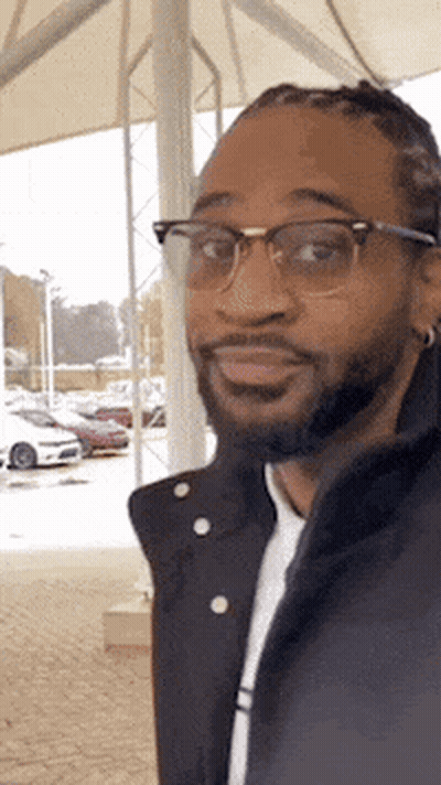 Bearded Man In Glasses And Black Jacket Standing In Parking Lot GIF