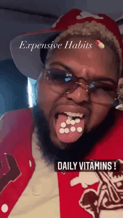 Bearded Man In Glasses And Red Jacket Holding Pills In Mouth GIF
