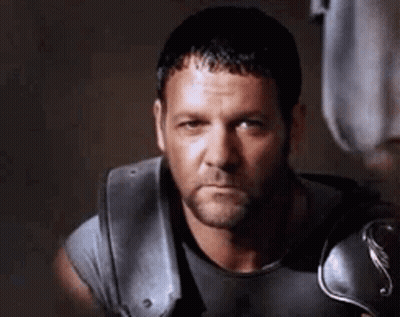 Bearded Man In Gray Shirt And Armor Looking At Camera GIF