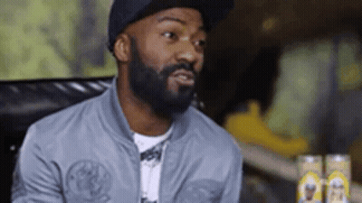 Bearded Man In Hat And Jacket Sitting At Table GIF