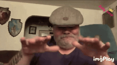 Bearded Man In Hat Sitting With Outstretched Hands GIF