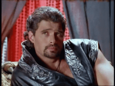 Bearded Man In Leather Vest Sitting On Couch GIF