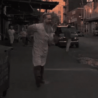 Bearded Man In White Apron Walking Down Street GIF