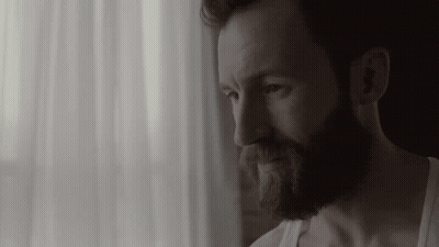 Bearded Man In White Tank Top Looking Out Window GIF