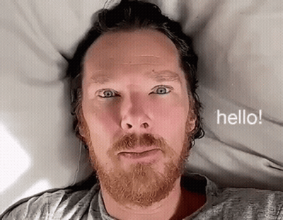 Bearded Man Laying On Bed Saying Hello GIF