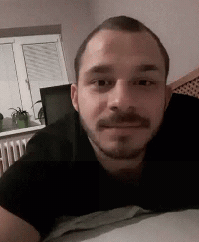 Bearded Man Laying On Bed Smiling At Camera GIF