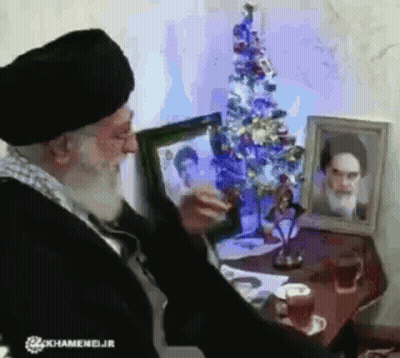 Bearded Man Looking At Picture Near Christmas Tree GIF