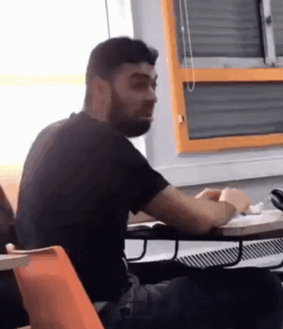 Bearded Man Sitting At Desk In Front Of Orange Window GIF