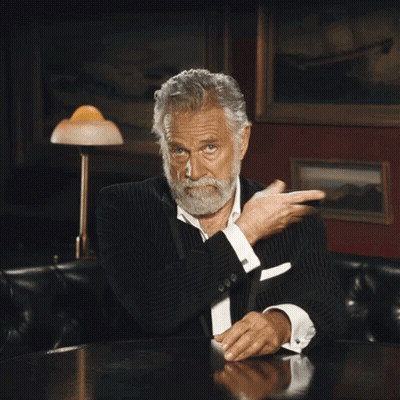 Bearded Man Sitting At Table With Hand On Chest GIF