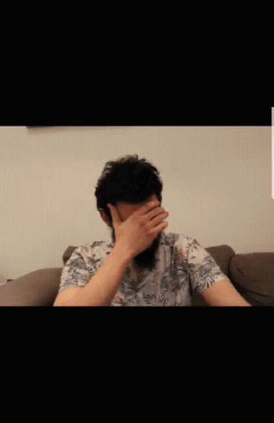 Bearded Man Sitting On Couch With Hands On Face GIF