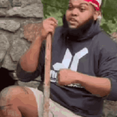 Bearded Man Sitting On Rock Holding Stick GIF