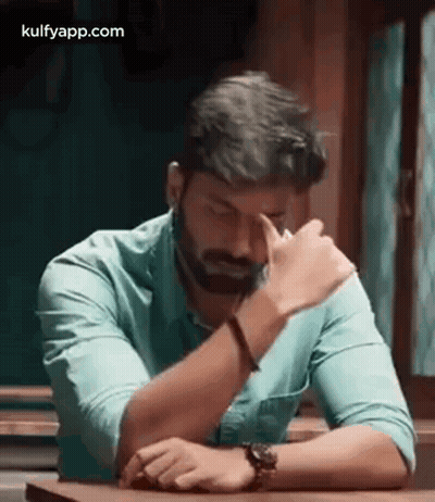 Bearded Man Sitting With Hands On Forehead GIF
