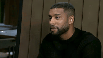 Bearded Man Smiling In Chair In Front Of Wooden Wall GIF