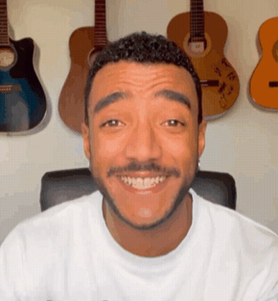 Bearded Man Smiling In Front Of Guitar Wall GIF