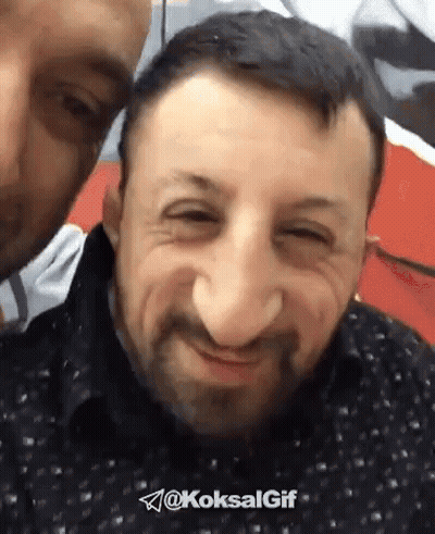 Bearded Man Smiling While Another Man Looks On GIF