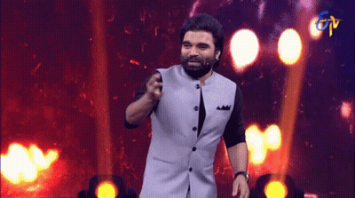 Bearded Man Standing On Stage In Front Of TV Logo GIF
