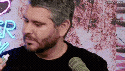 Bearded Man Talking Into Microphone in Front of Neon R Sign