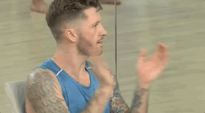 Bearded Man With Tattoos In Blue Tank Top Sitting In Front Of Mirror GIF
