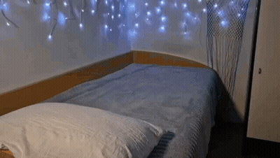 Bed With Blue Blanket And White Pillow Under Christmas Lights GIF