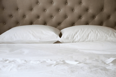 Bed With White Sheets Under Buttoned Headboard GIF