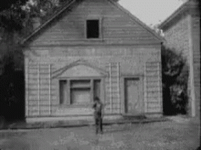 Black And White Man In Front Of Small Wooden House GIF