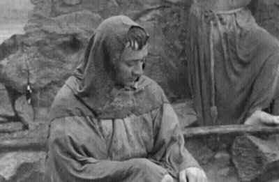 Black And White Man In Hooded Cloak Sitting On Ground GIF