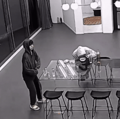 Black And White Man Standing Next To Table With Water Bottle GIF