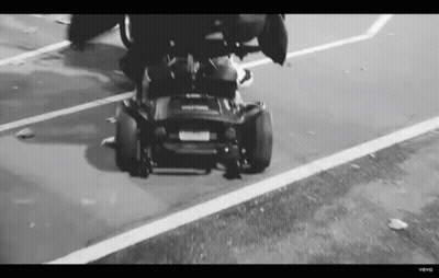 Black And White Person Driving Lawn Mower Down Street GIF
