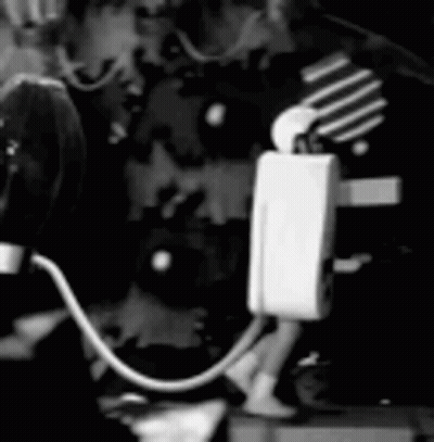Black And White Person Standing Next To Microphone And Light Bulb GIF