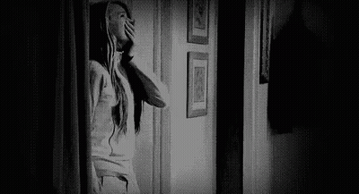 Black And White Photo Of Woman Looking Out Door In Hallway GIF