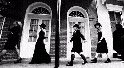 Black And White Photo Of Women Walking Down Sidewalk In Front Of Brick Building GIF