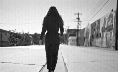 Black And White Woman Walking Past Graffiti Wall GIF