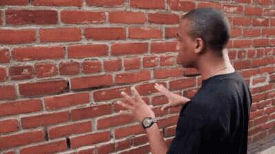 Black Shirt Man By Red Brick Wall GIF