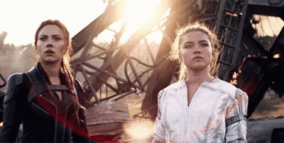 black widow and white widow are standing next to each other in front of a destroyed building .